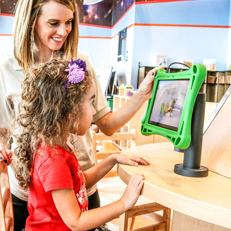 Teacher helping pre-school girl with tablet learning